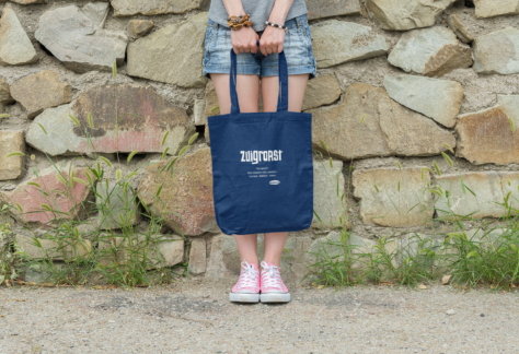 Eine Junge Frau lent an einer Mauer und hält eine OstSeele-Tasche vor ihren Beinen.