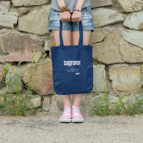 Eine Junge Frau lent an einer Mauer und hält eine OstSeele-Tasche vor ihren Beinen.