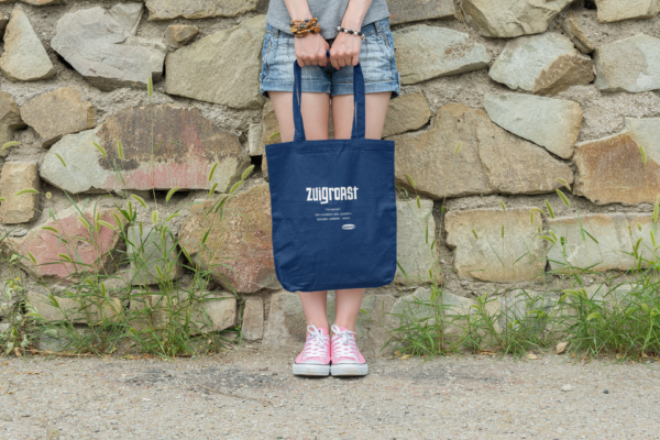 Eine Junge Frau lent an einer Mauer und hält eine OstSeele-Tasche vor ihren Beinen.