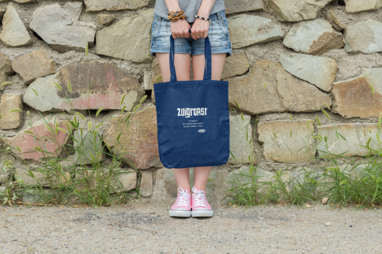 Eine Junge Frau lent an einer Mauer und hält eine OstSeele-Tasche vor ihren Beinen.